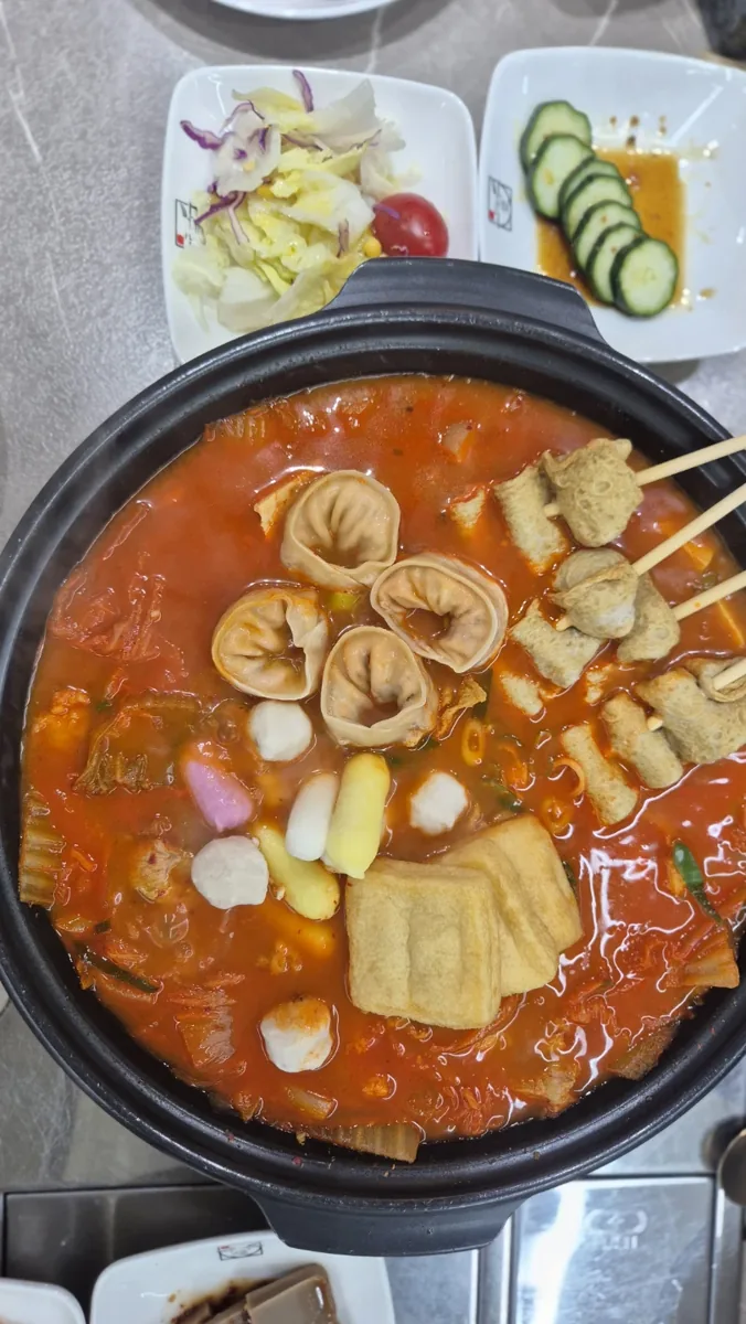 쌀밥애 찌개담다 김치찌개에 만두와 어묵, 떡, 꼬치류 속재료를 추가한 음식 사진