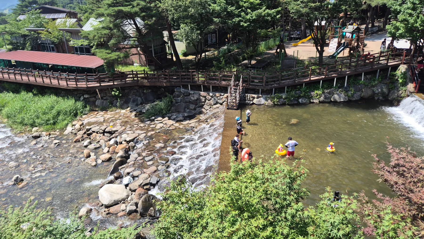 카페 날망 아래 계곡과 데크, 놀이터가 함께 보이는 풍경